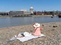 A woman sits in the warm weather and sunshine on the southern bank of the River Thames in London.