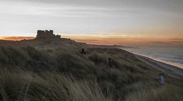 Children run through the sand dunes as the sun sets behind Bamburgh Castle