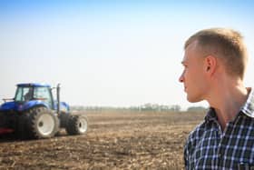 Young man in a field and a tractor on a background. Concept of agriculture and field works.