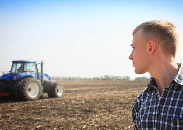 Young man in a field and a tractor on a background. Concept of agriculture and field works.