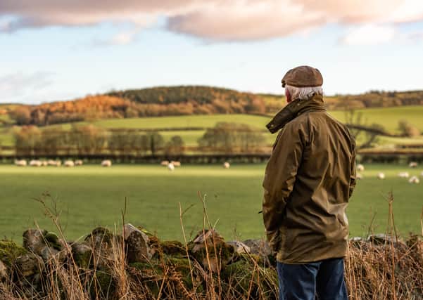 A man with his back to camera wearing a waxed jacket and flat tweed cap looking across a field