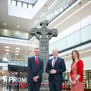 Communities Minister Gordon Lyons with Acting Director of PRONI David Huddleston and HERoNI’s Rhonda Robinson stand at the reconstructed Donaghmore high cross currently being exhibited at PRONI