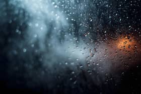 Detailed close up of water condensation forming numerous clear droplets on a dark wet glass window pane