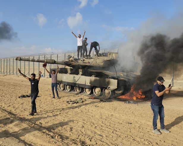 Palestinians celebrate by a destroyed Israeli tank at the Gaza Strip fence east of Khan Younis Saturday, Oct. 7, 2023. The militant Hamas rulers of the Gaza Strip carried out an unprecedented, multi-front attack on Israel at daybreak Saturday, firing thousands of rockets as dozens of Hamas fighters infiltrated the heavily fortified border in several locations by air, land, and sea and catching the country off-guard on a major holiday (AP Photo/Hassan Eslaiah)