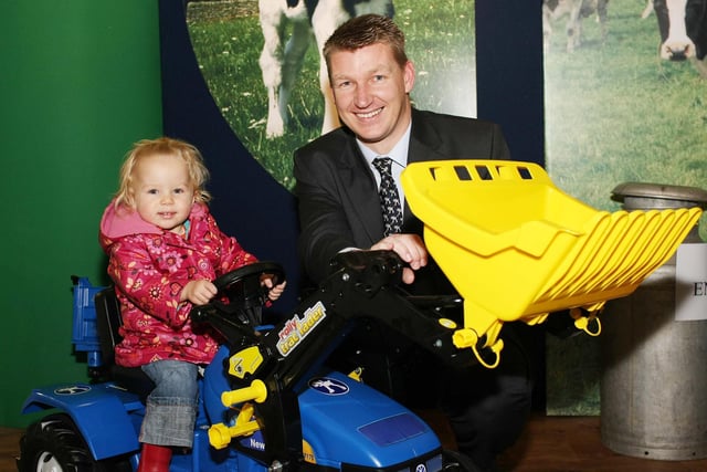 One year old Aimiee Farrell, Lisnaskea, shows Gordon Donaldson, John Thompson and Son's, the right way to drive. The tractor was a prize in the raffle on the John Thompson and Son's stand at the Winter Fair.